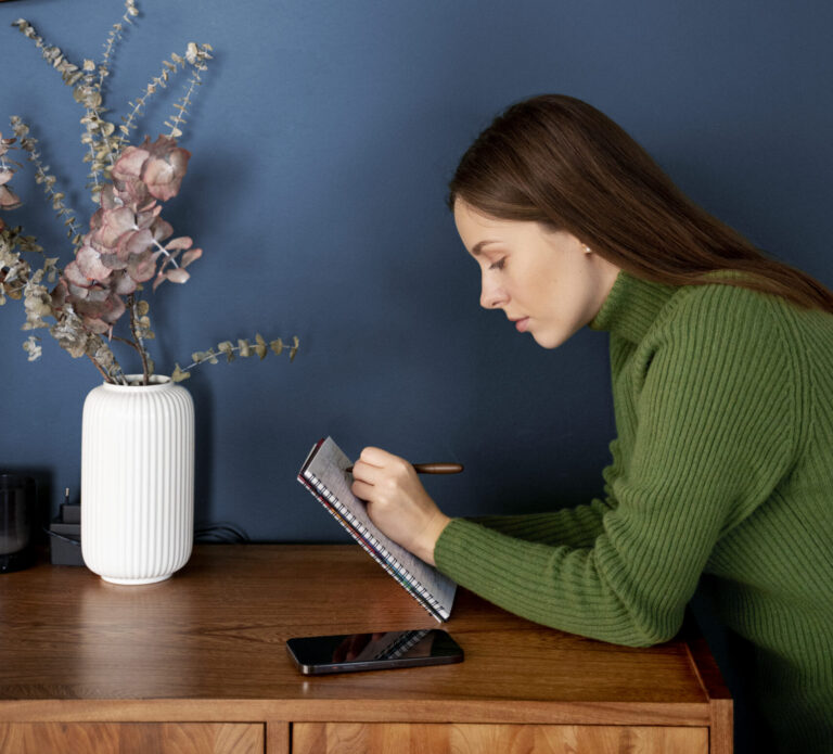 Woman writing in a notebook next to her smartphone, practicing minimalism through intentional planning
