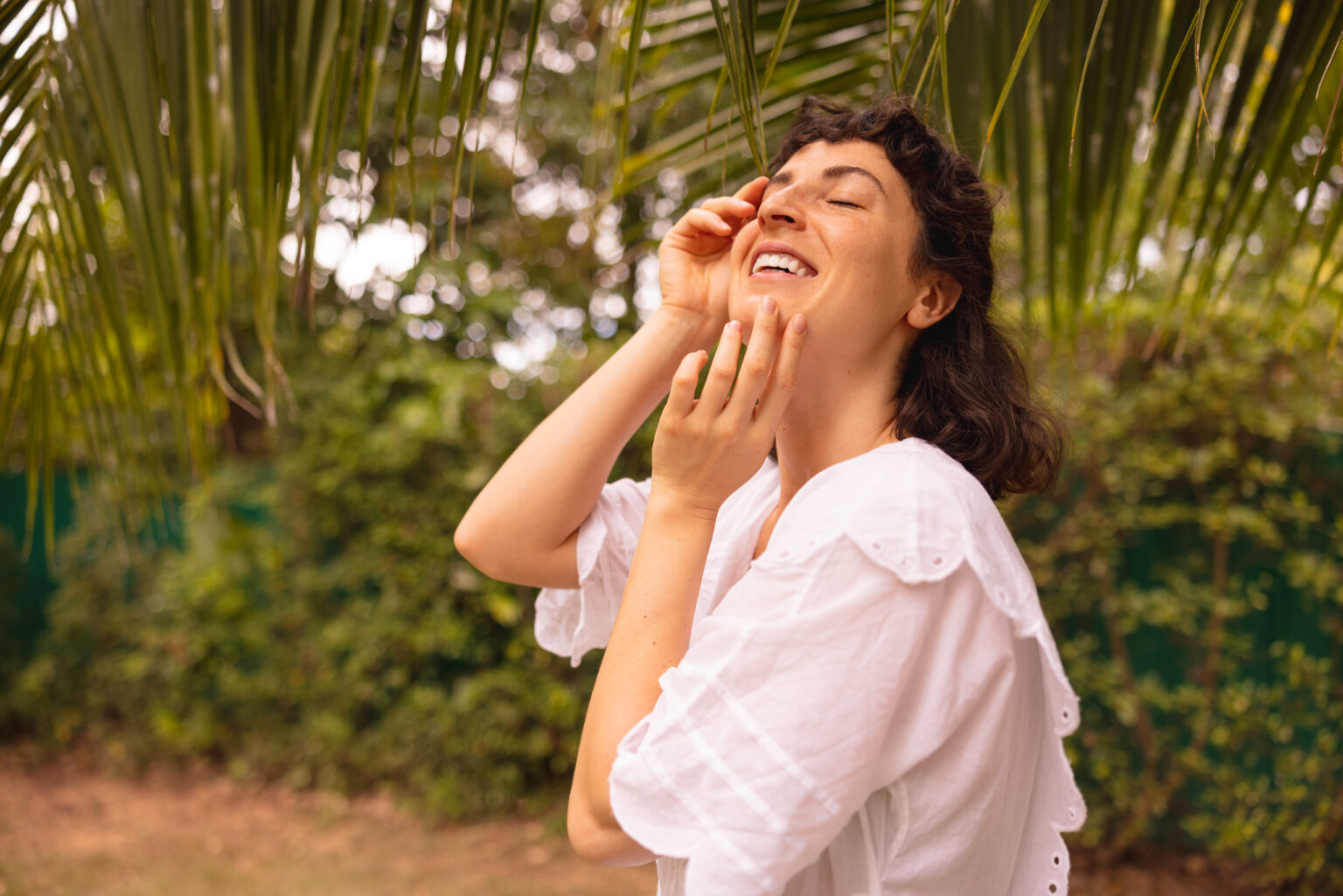 Young woman smiling with closed eyes, gently touching her face—symbolizing microbiome skin care and naturally healthy skin